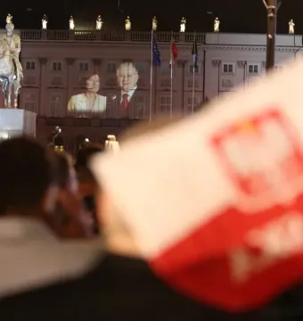 The Prince Józef Poniatowski Monument lit in red at night in front of a grand building with projected images on its facade.