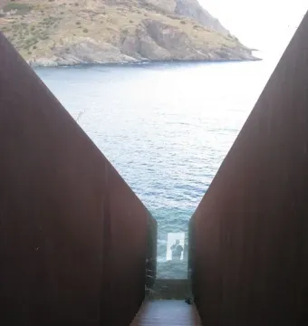 Steep rust-colored metal staircase descending between tall walls at the Walter Benjamin Memorial in Portbou.
