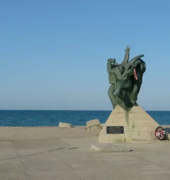 Bronze monument of the Eupatoria Assault showing three dynamic figures on a stone pedestal by the sea.