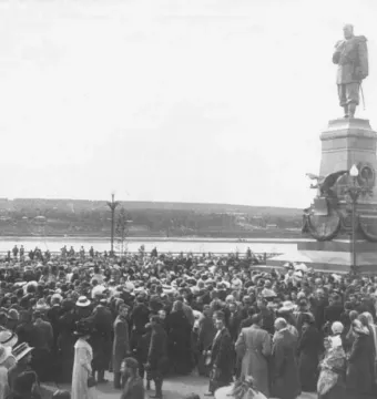 The Monument of Alexander III stands on a decorated multi-tiered pedestal with a large crowd gathered around it.