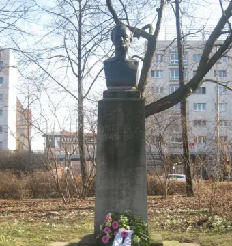 Richard Wagner bust on a weathered stone pedestal with a floral wreath at the base in a park