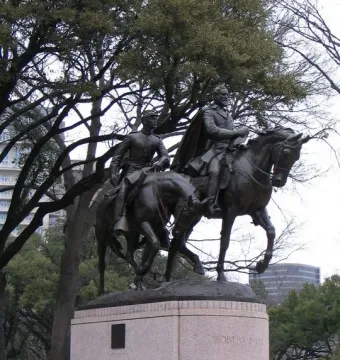 Robert E. Lee equestrian statue on a stone pedestal with trees and modern buildings in the background.
