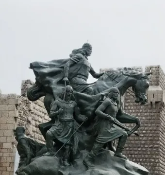 Saladin equestrian statue with armed figures in front of the Citadel walls in Damascus.