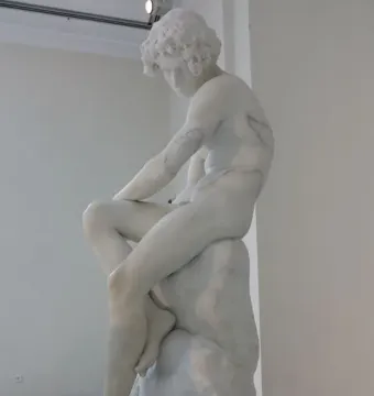 The Exiled, a white marble sculpture of a bowed youthful figure seated on rock.