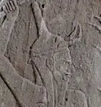 Profile close-up of Baal with a horned helmet and raised arm.