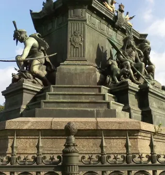 Ornate bronze and stone base of the Dom Pedro I Equestrian Statue with sculptural figures, including a crouching figure with a bow and a seated figure holding a spear.
