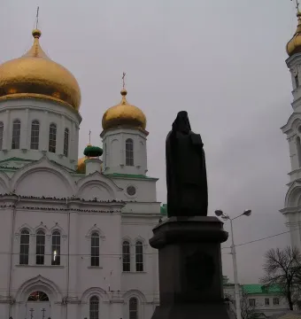 Monument to Dimitry of Rostov in front of a white Orthodox cathedral with golden domes and a bell tower.