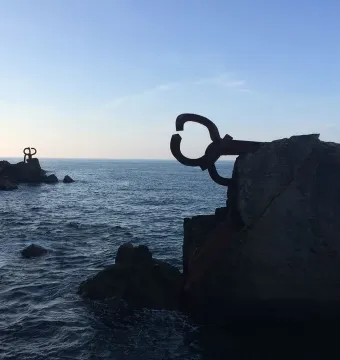 Peine del Viento sculptures silhouetted on rocky coastline beside a dark, choppy sea