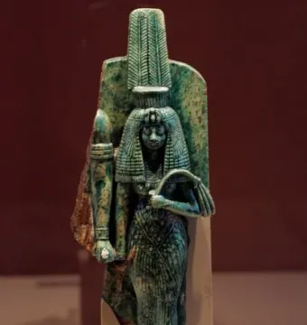 Greenish-blue statue of Queen Tiye wearing a tall ornate headdress and long textured garment, holding objects in both hands.