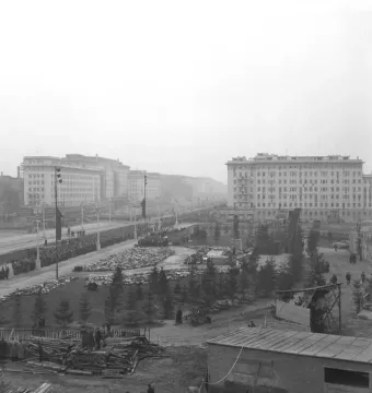 A large Stalin monument plinth stands in a broad square beside an avenue lined with crowds and administrative buildings.
