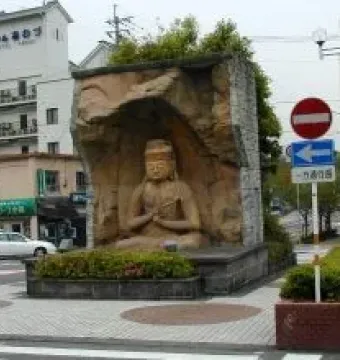 Usuki Stone Buddha seated in a carved grotto structure in a paved urban square.