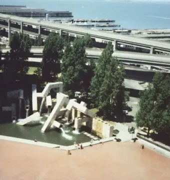 Vaillancourt Fountain in a plaza with concrete blocks and water, with trees and freeway overpasses in the background.
