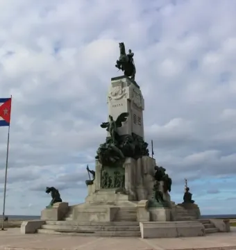 Antonio Maceo Monument with bronze figures and an equestrian statue at the top, with a Cuban flag and the sea behind it.