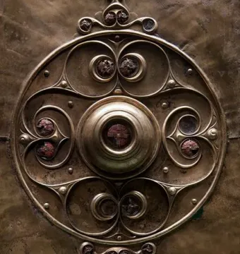 Close-up of the Battersea Shield showing a central boss, swirling bronze patterns, and circular inlays.
