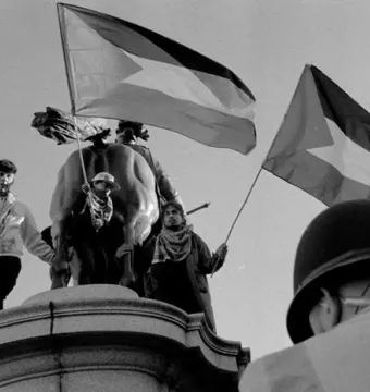 Rear view of the Duke of Cambridge equestrian statue with several people on the pedestal holding flags.