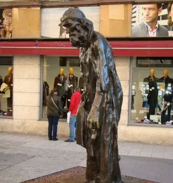 Eustache de Saint Pierre bronze sculpture of a bearded man in long robes standing on a stone base beside storefront windows