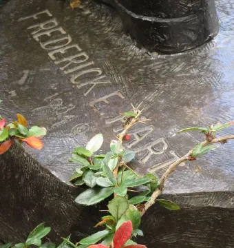 Close-up of the Frederick F. Hart inscription on the dark, textured base of The Three Soldiers, partly covered by thorny foliage and red berries.