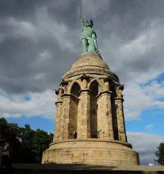 Hermannsdenkmal monument with a warrior statue holding a sword aloft against a dramatic cloudy sky.