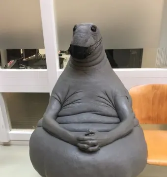 Homunculus Loxodontus sculpture wearing a black face mask and resting its clasped hands on its belly.