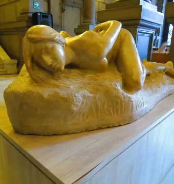 Malgré Tout, a stone sculpture of a reclining woman with flowing hair on a wooden pedestal.