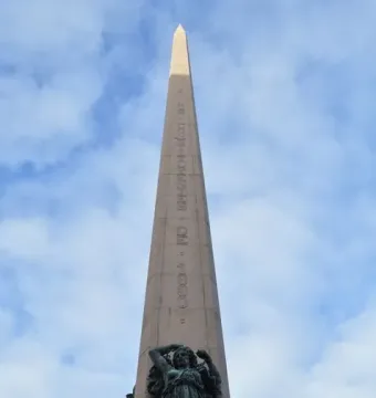 The Obelisk of Montevideo rises against a blue sky, with bronze figures at its base.
