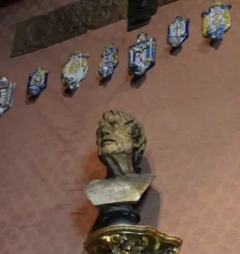 Pseudo-Seneca bronze bust of an older man with a gaunt face and upward gaze, mounted on a pedestal against a patterned wall.