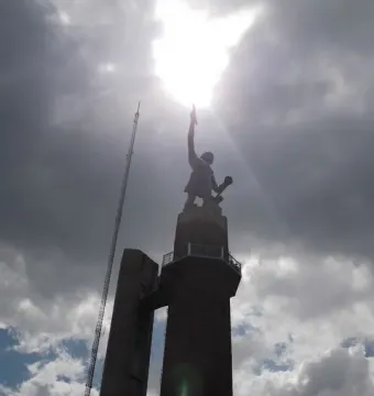 The Vulcan statue appears as a dark silhouette atop a tall brick pedestal, backlit by the sun in a cloudy sky.