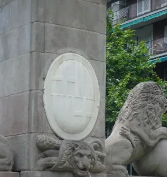 Close-up of the Fountain of Hercules showing a carved lion head spouting water beside a marble plaque and stone lion sculpture.