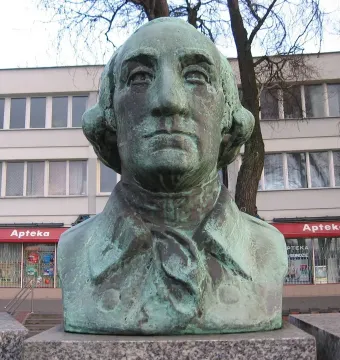 Teal-patinated bust of George Washington with a building and Apteka storefront behind it.