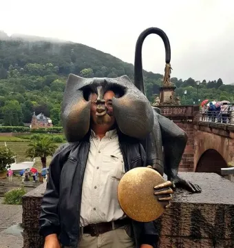 Person posing behind the Heidelberg Bridge Monkey sculpture with their face placed in the hollow head opening.