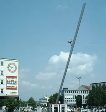 Himmelsstürmer sculpture on a tilted pole against a blue sky above an urban square in Kassel