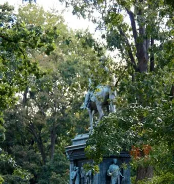 Major General John A. Logan equestrian statue on an ornate pedestal in a park, with trees and a person sitting on a bench nearby.