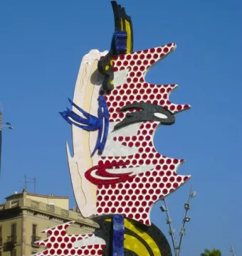 The Face of Barcelona sculpture with a red dotted pop-art pattern against a clear blue sky.