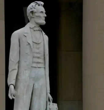 Marble statue of Abraham Lincoln standing in a suit with one hand resting on a bundle of rods.