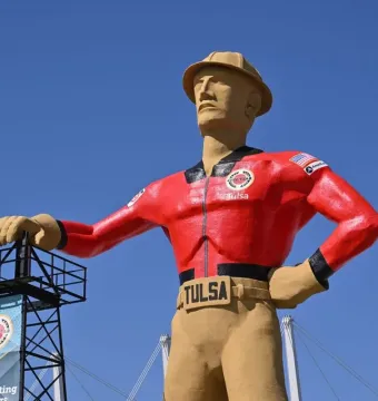 Golden Driller statue in Tulsa wearing a red jacket and tan hard hat beside a black metal tower.