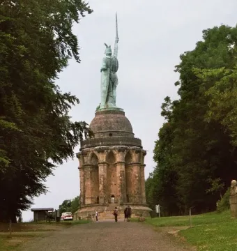 Hermannsdenkmal, a green-patina warrior statue holding a sword high atop a stone pedestal with arched openings, surrounded by trees.