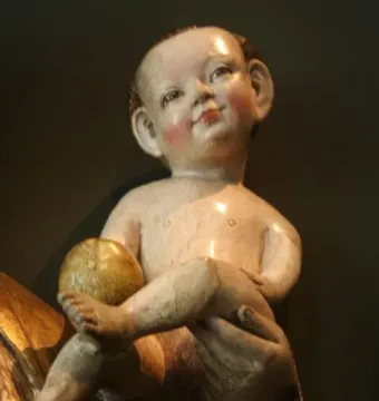 Rosy-cheeked baby figure holding a golden orb on a dark textured surface.