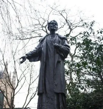 Pankhurst Memorial statue on a tiered stone pedestal, with the figure’s arm outstretched outdoors among bare trees.
