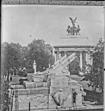 Royal Artillery Memorial with a large howitzer on a tiered stone base, detailed reliefs, and draped figures, with ladders and workers nearby.