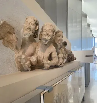 Trisomatos Typhon limestone figures displayed on a museum plinth, including a winged bearded torso.