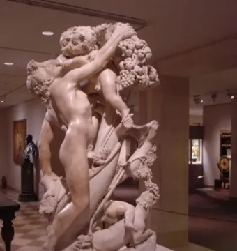 Marble sculpture of A Faun Teased by Children showing a nude faun with children playing around him and holding grapes overhead.