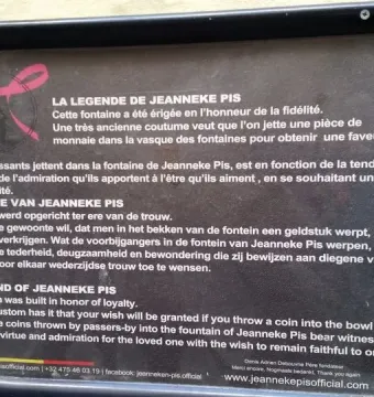A rectangular sign about the legend of Jeanneke Pis mounted on a textured wall.