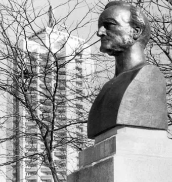 Richard Wagner bust on a stone base with his name carved into it, with bare branches and a tall apartment building in the background.