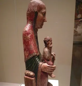 Virgin from Ger wooden carving shown in profile, with a robed figure holding a smaller figure on its lap.