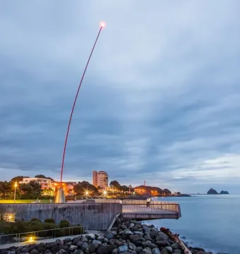 Wind Wand on a coastal promenade at dusk, lit at the tip against a cloudy evening sky.