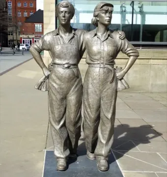Women of Steel bronze sculpture of two women standing arm in arm in work clothes.