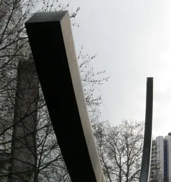 Bernar Venet’s Arc de 124,5° sculpture rising over a grassy area with bare trees and city buildings in the background.