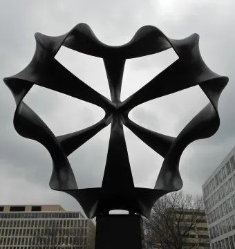 Continuum sculpture with dark, looping metal forms radiating from a central point against a cloudy sky.