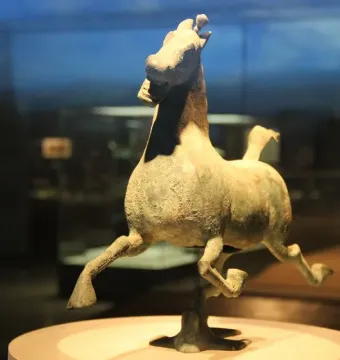 Weathered bronze Flying Horse of Gansu sculpture in a galloping pose on a pedestal inside a display case.