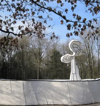Jardin d\'émail sculpture with a wavy white wall and abstract tree-like form among bare trees.